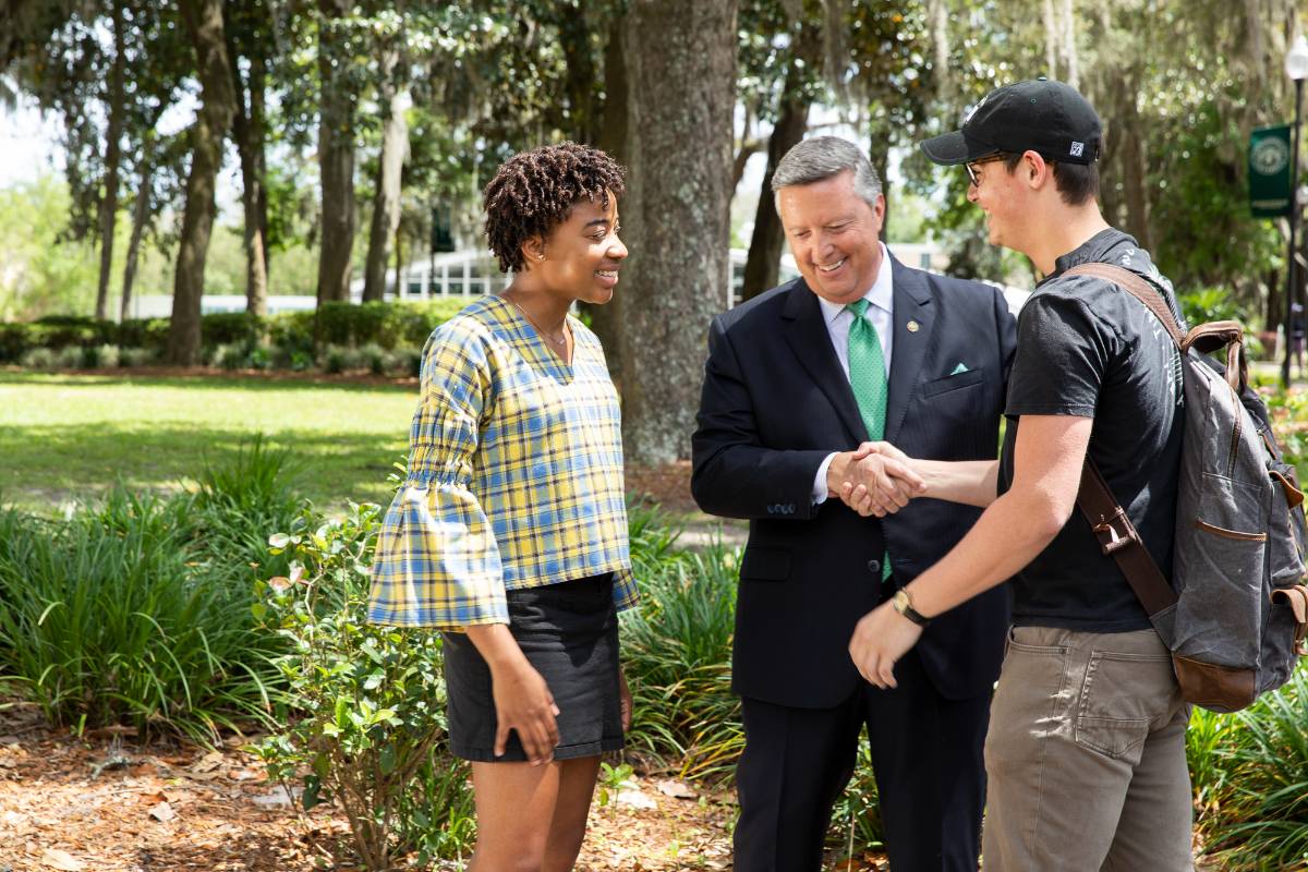 Two students talking with A1 President Tim Cost in courtyard on campus